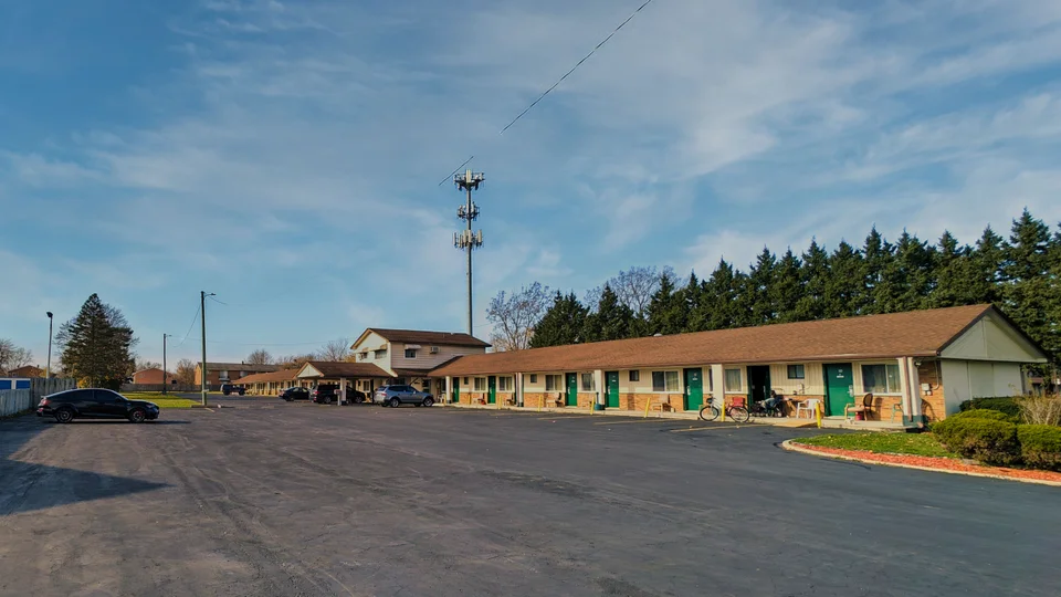 Delta Motel guest rooms with green doors, covered entrances, and a spacious paved parking lot under a blue sky